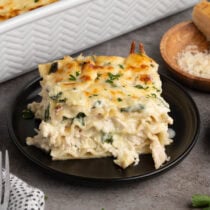 Plated slice of layered white chicken lasagna with spinach and melted cheese on a black plate.