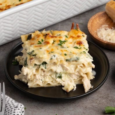 Plated slice of layered white chicken lasagna with spinach and melted cheese on a black plate.