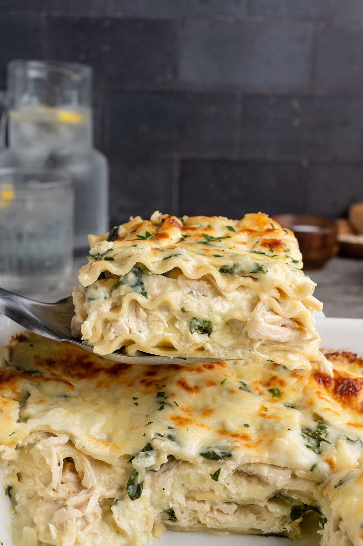 Slice of white chicken lasagna with spinach lifted from the baking dish, showing layered noodles and cheese.