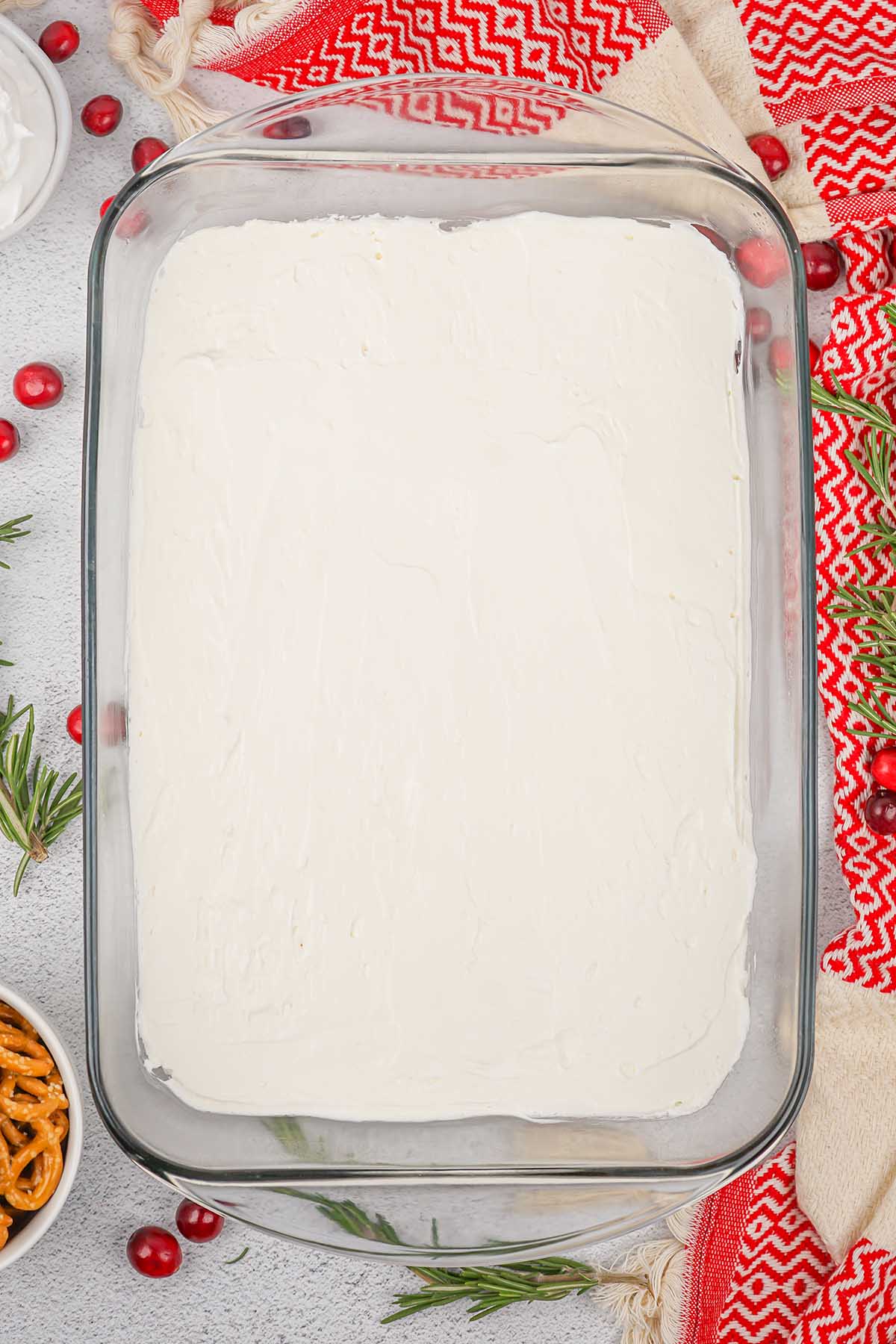 Creamy white cheesecake layer spread over the pretzel crust in a glass baking dish.