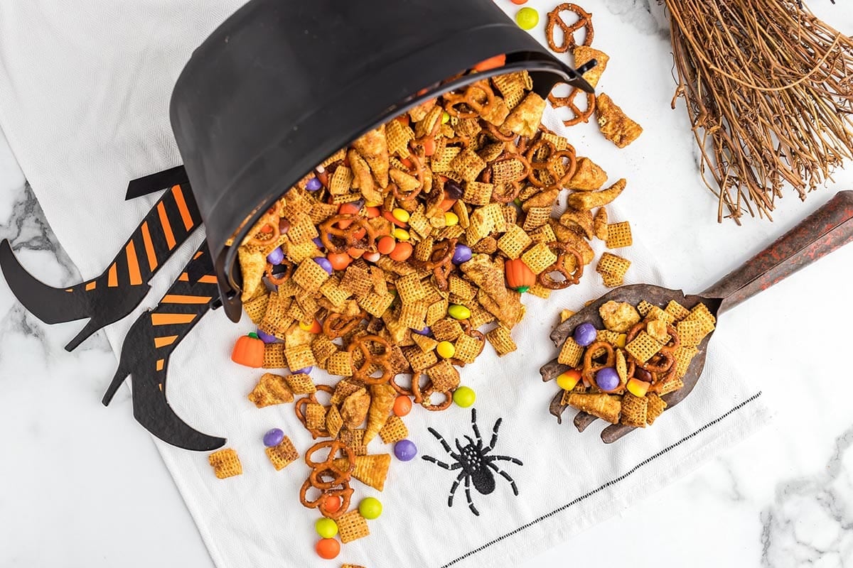 Halloween Chex mix spilling from a cauldron onto a spider napkin.
