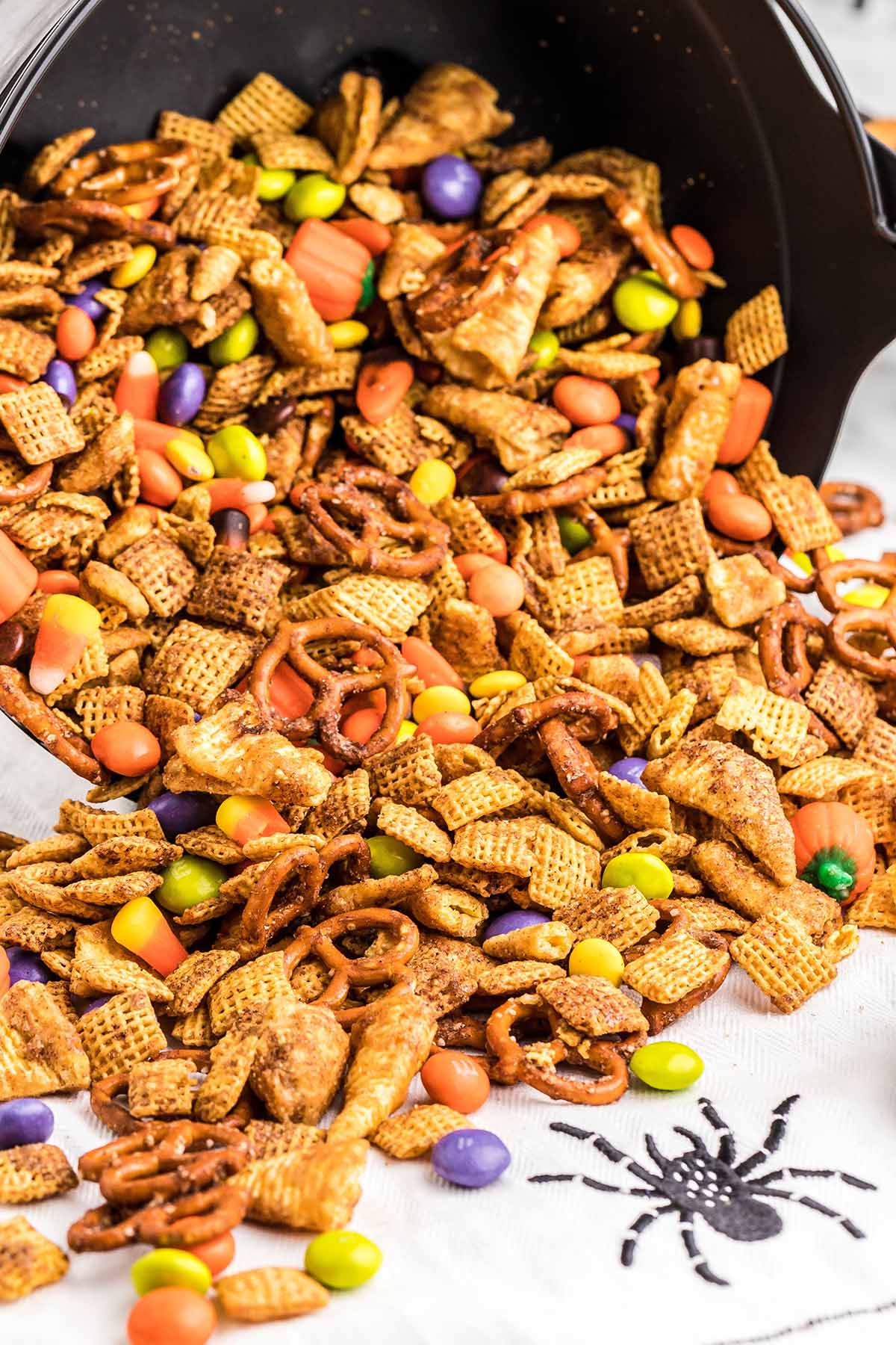 Halloween Chex mix spilling from a cauldron onto a spider napkin.
