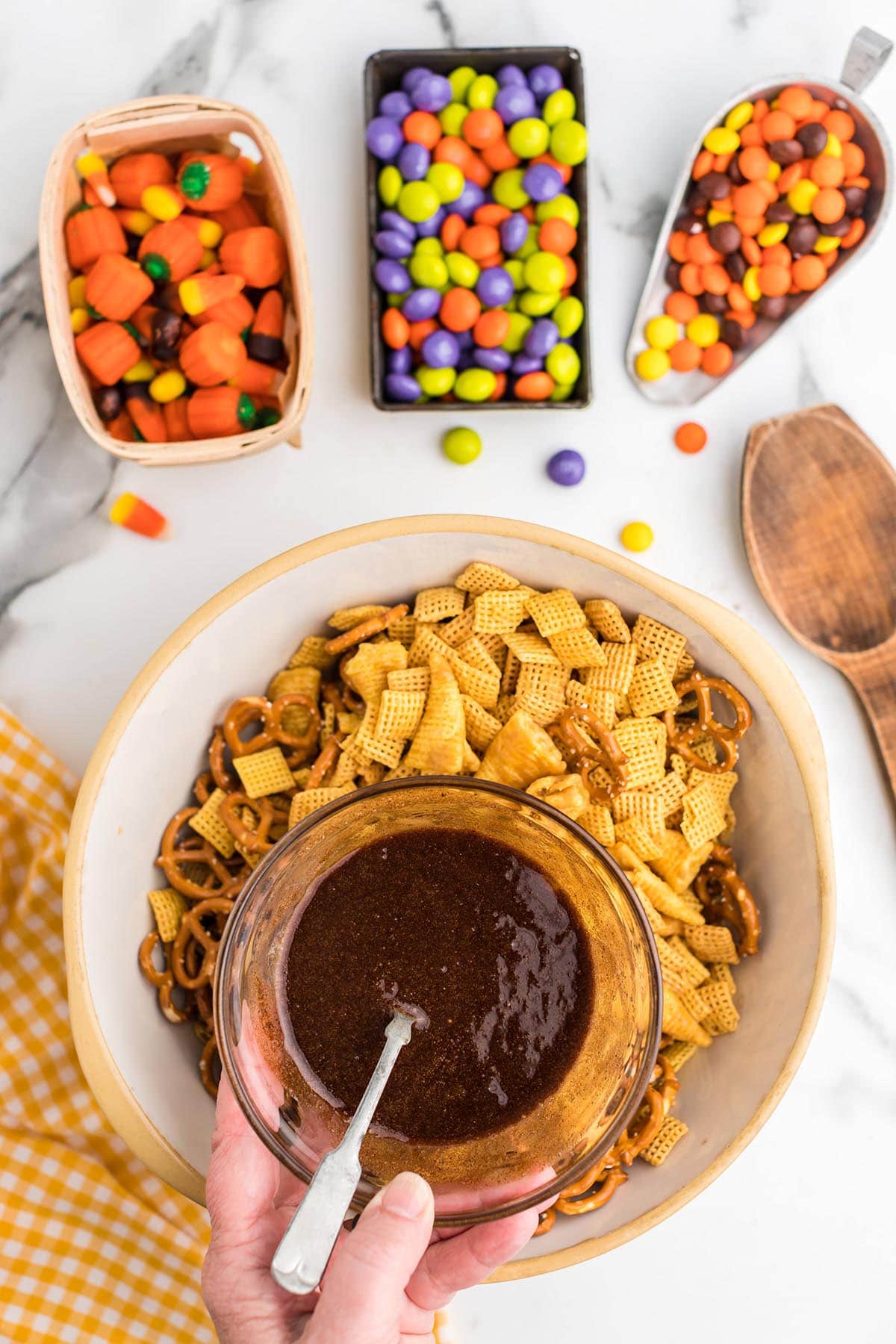 Hand pouring seasoning sauce over Chex mix and pretzels in a bowl.