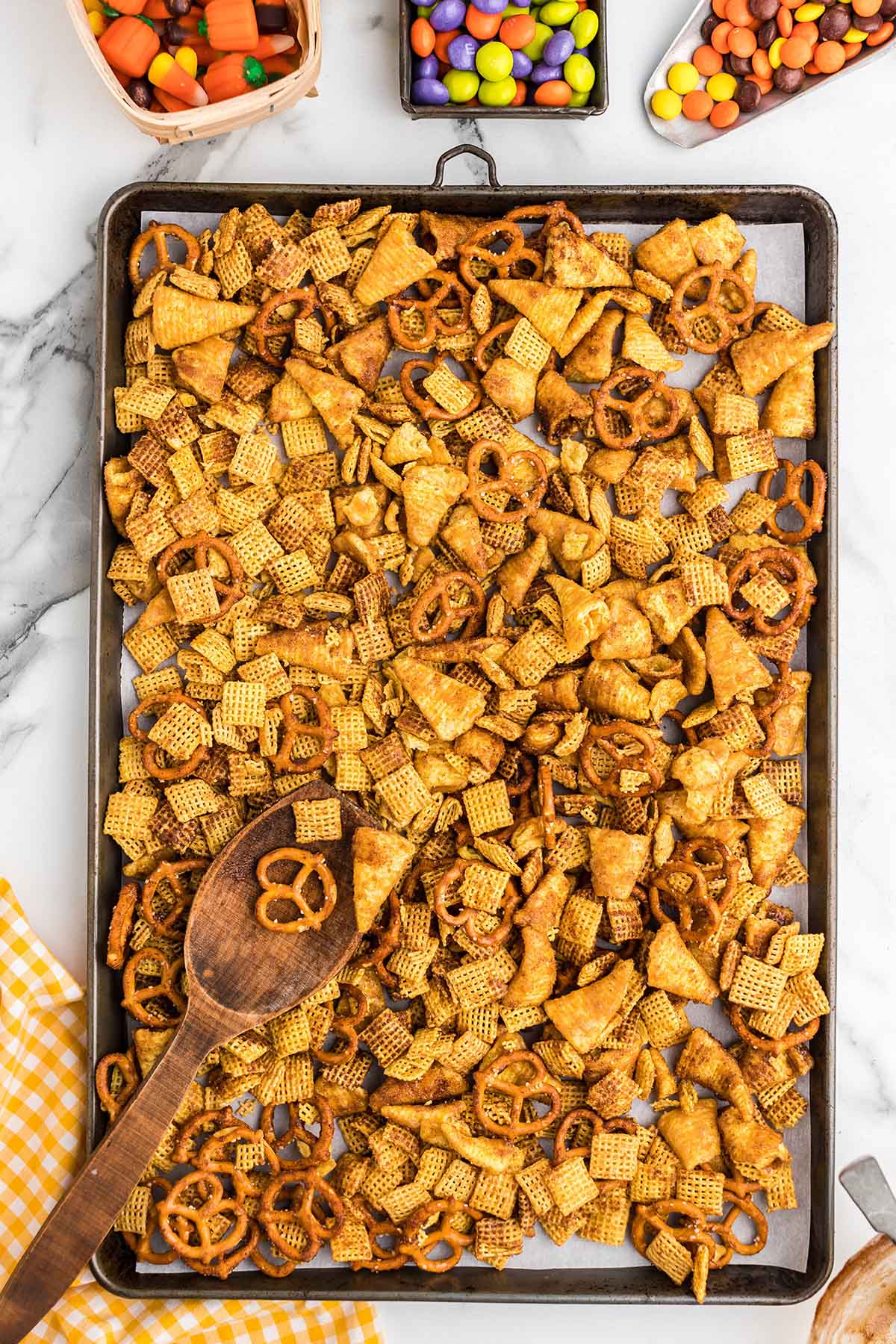 Halloween Chex mix spread on a baking sheet with a wooden spoon.