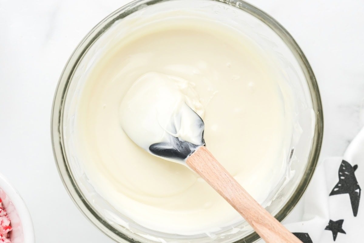 Melted white chocolate in a glass bowl with a spatula.