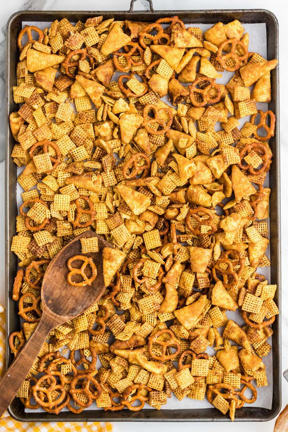 Pumpkin spice snack mix spread on a baking sheet with a wooden spoon.