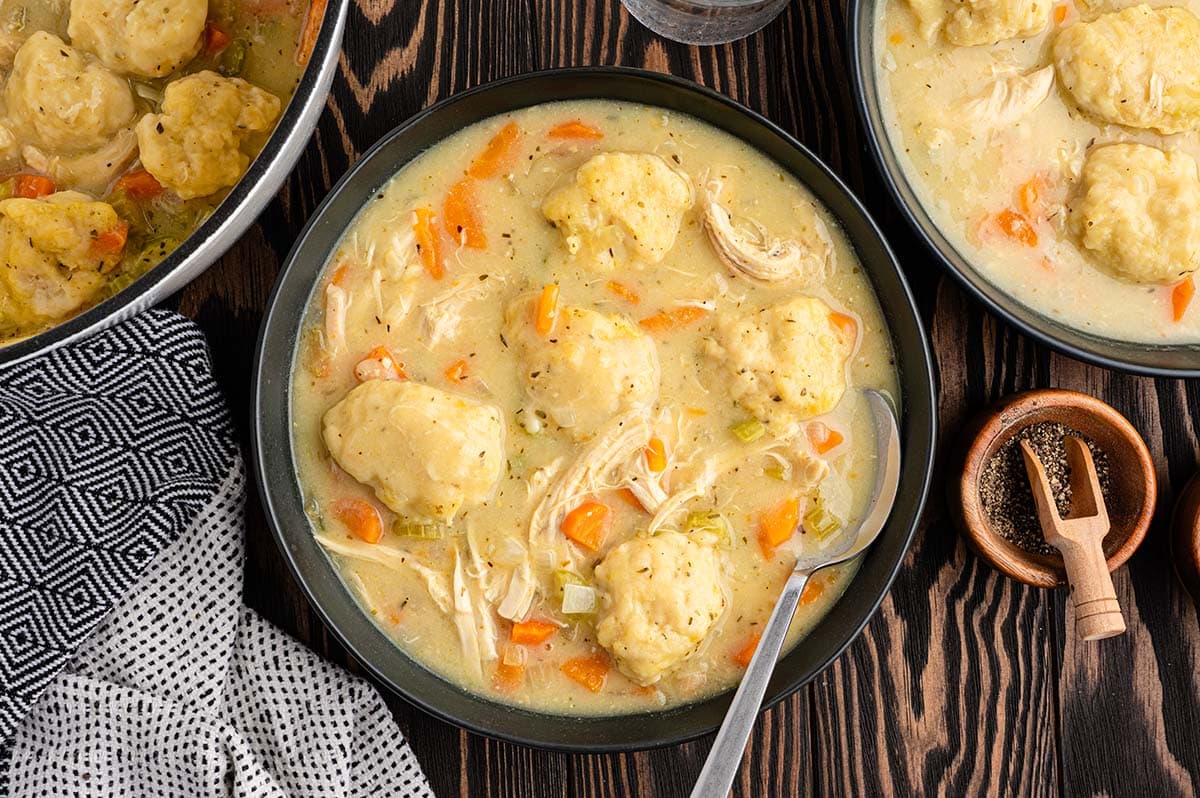 Bowl of chicken and dumplings with carrots and a spoon on a wooden table.