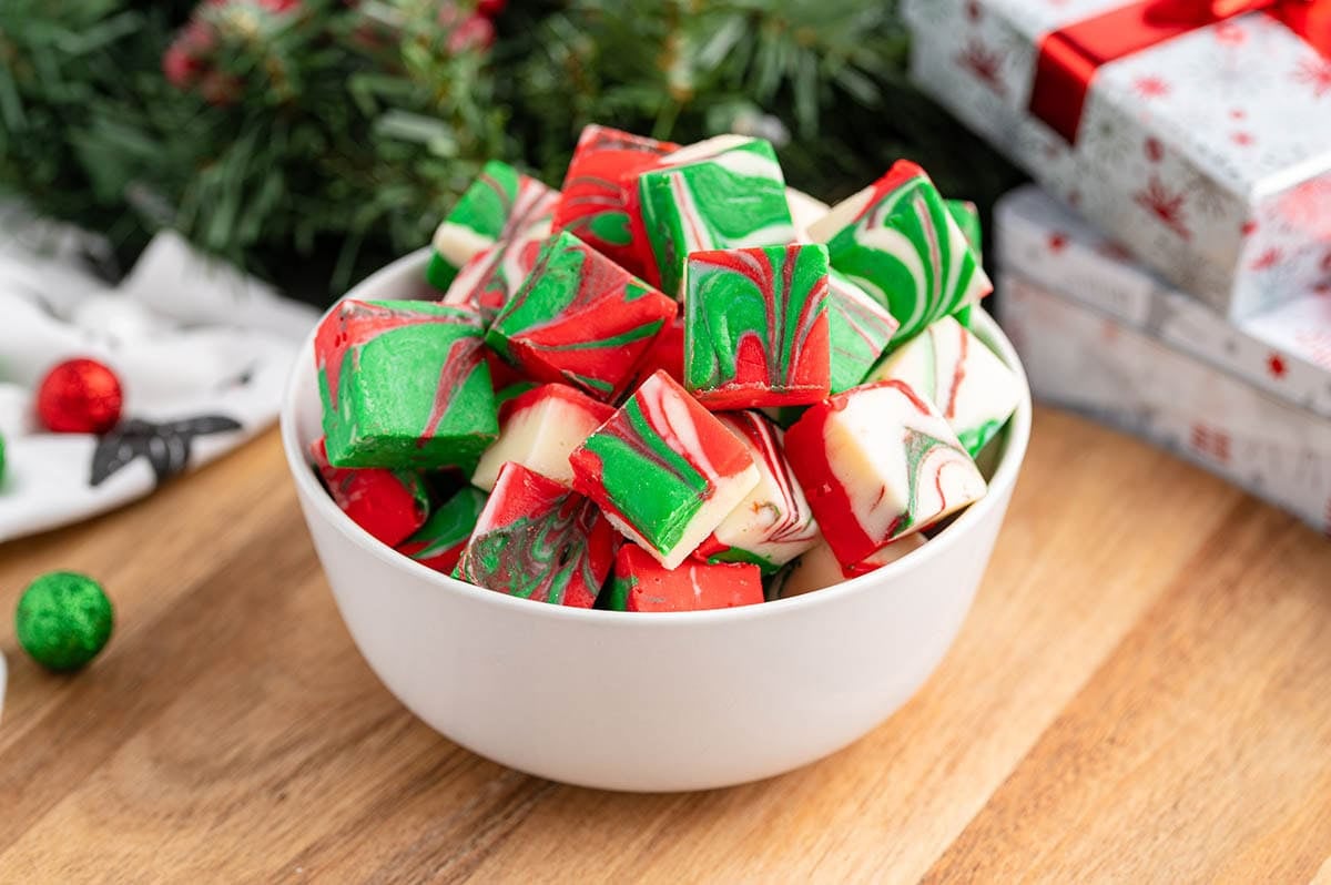 Squares of Christmas Fudge stacked on a white plate so the red, green and white swirl shows on the cut sides.