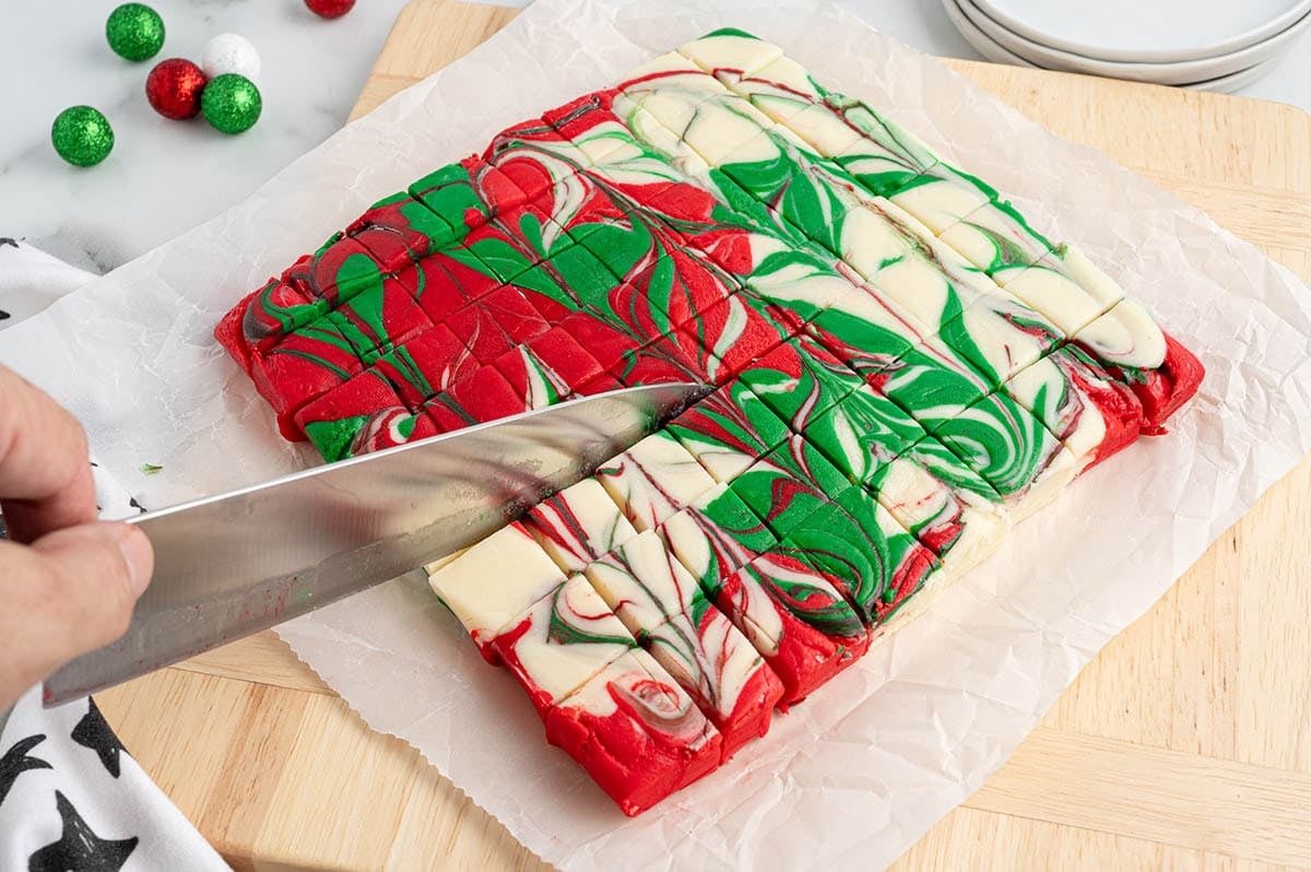 Swirled Christmas fudge being cut into squares on parchment paper.