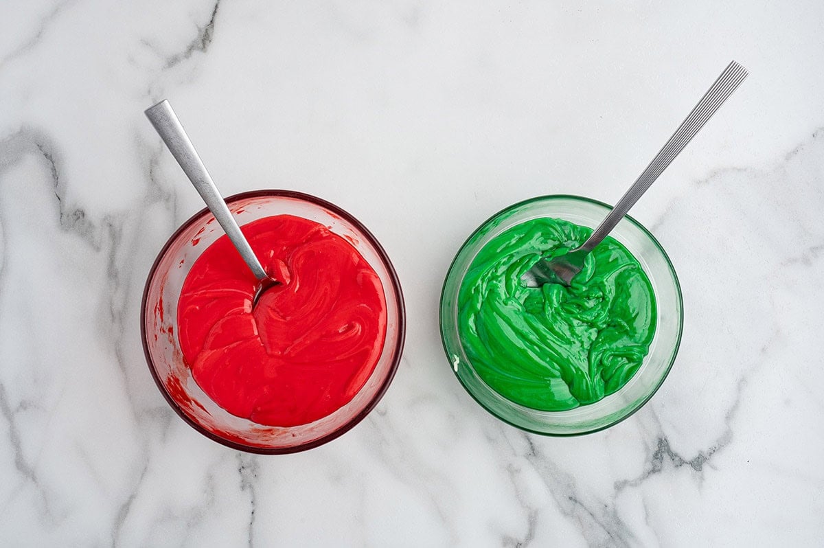 Two bowls of fudge mixture, one dyed red and one dyed green, with spoons.
