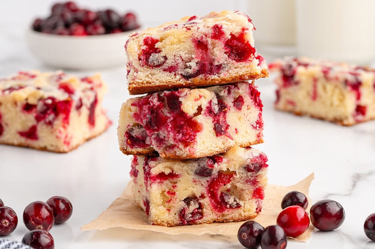 Three cranberry cake squares stacked with more slices in the background.
