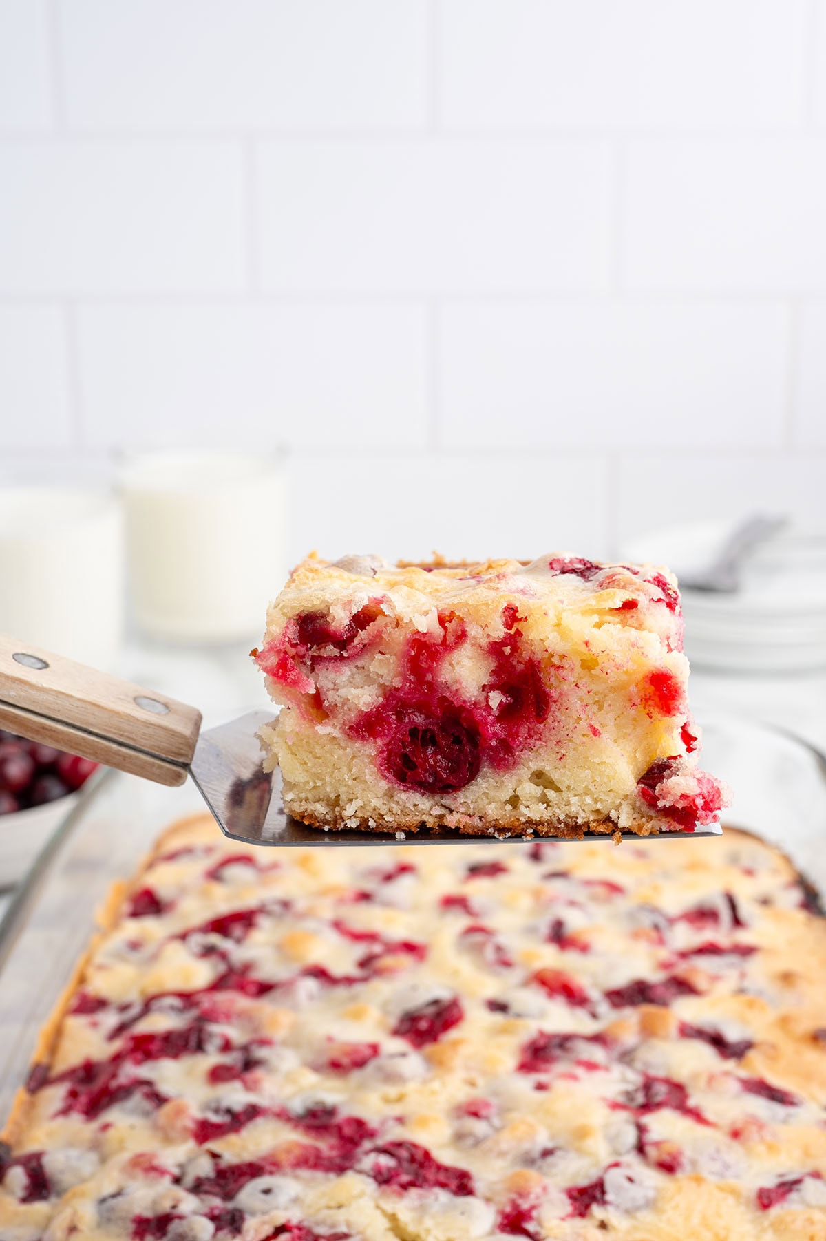 Slice of cranberry cake lifted with a spatula over the full baked cake.