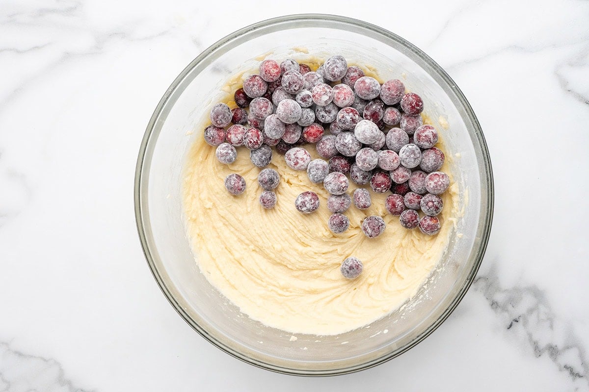 Frozen cranberries added to cake batter in a bowl.
