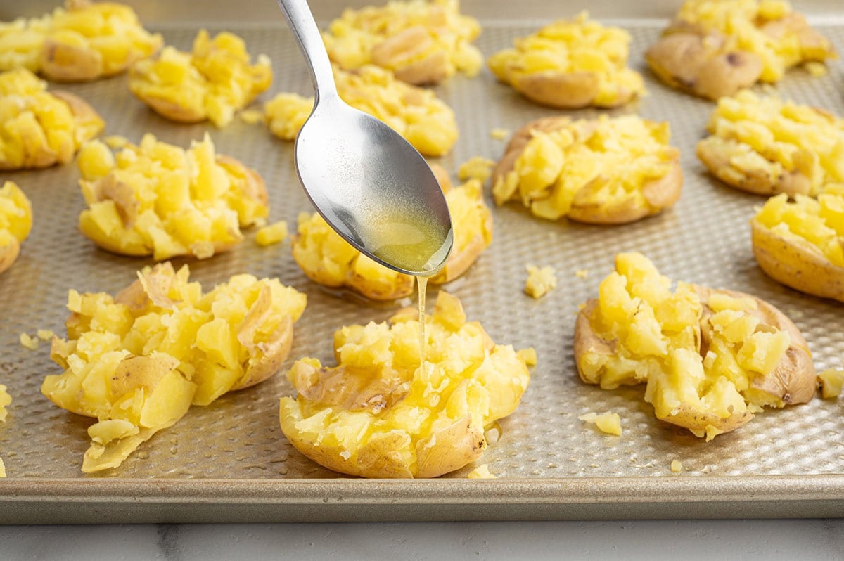 Spoon drizzling oil over smashed potatoes on a baking sheet.