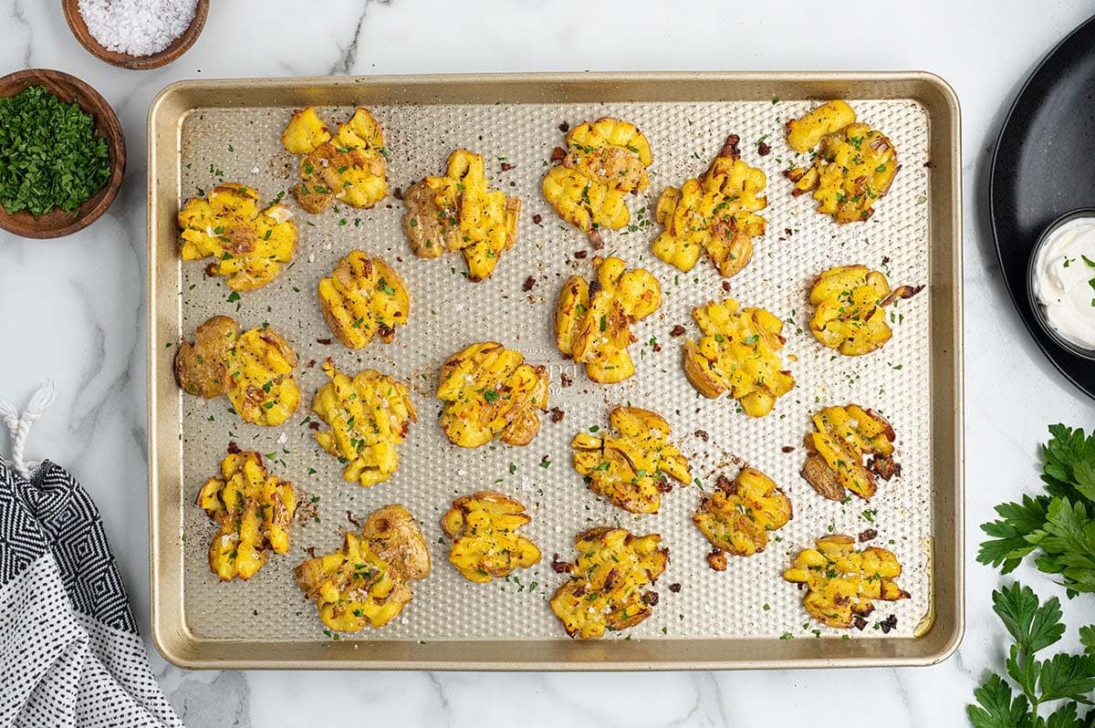 Overhead view of crispy smashed potatoes on a baking sheet.