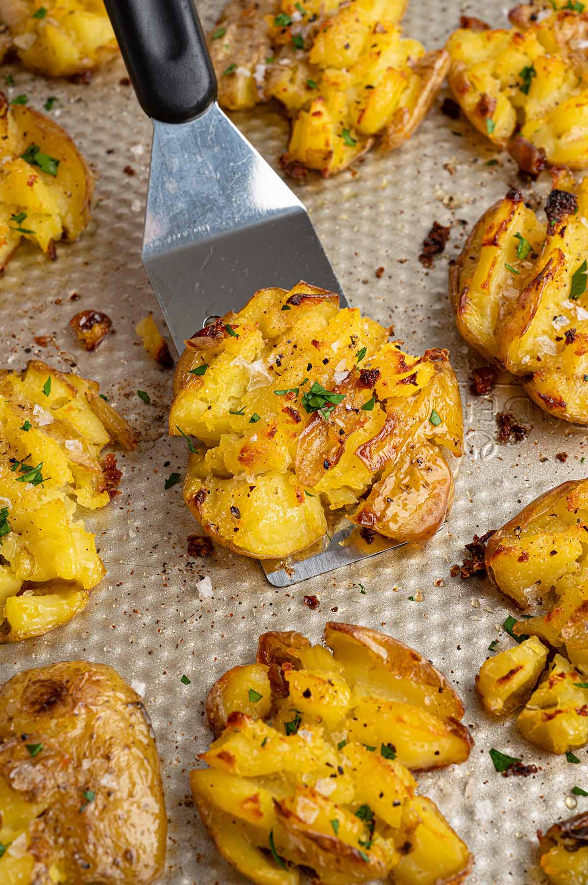 Spatula lifting a crispy smashed potato off a baking sheet.