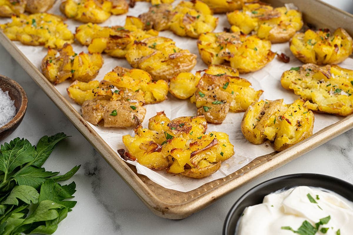 Crispy smashed potatoes on a baking sheet with parsley and sour cream.