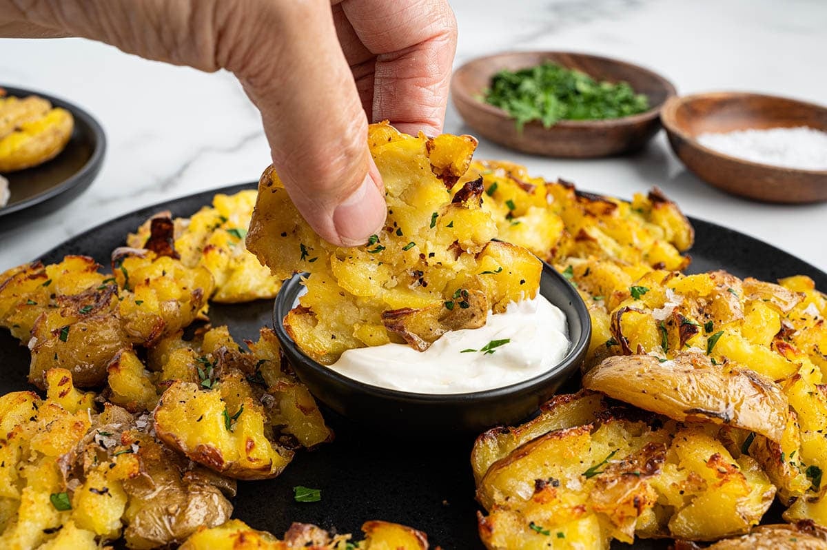 Hand dipping a crispy smashed potato into sour cream.