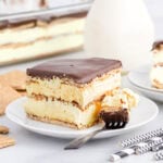Slice of eclair cake with a bite on a fork, showing layers of graham cracker, pudding, and chocolate topping.