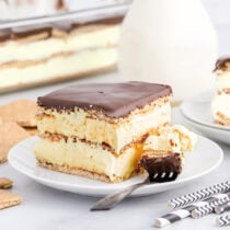 Slice of eclair cake with a bite on a fork, showing layers of graham cracker, pudding, and chocolate topping.