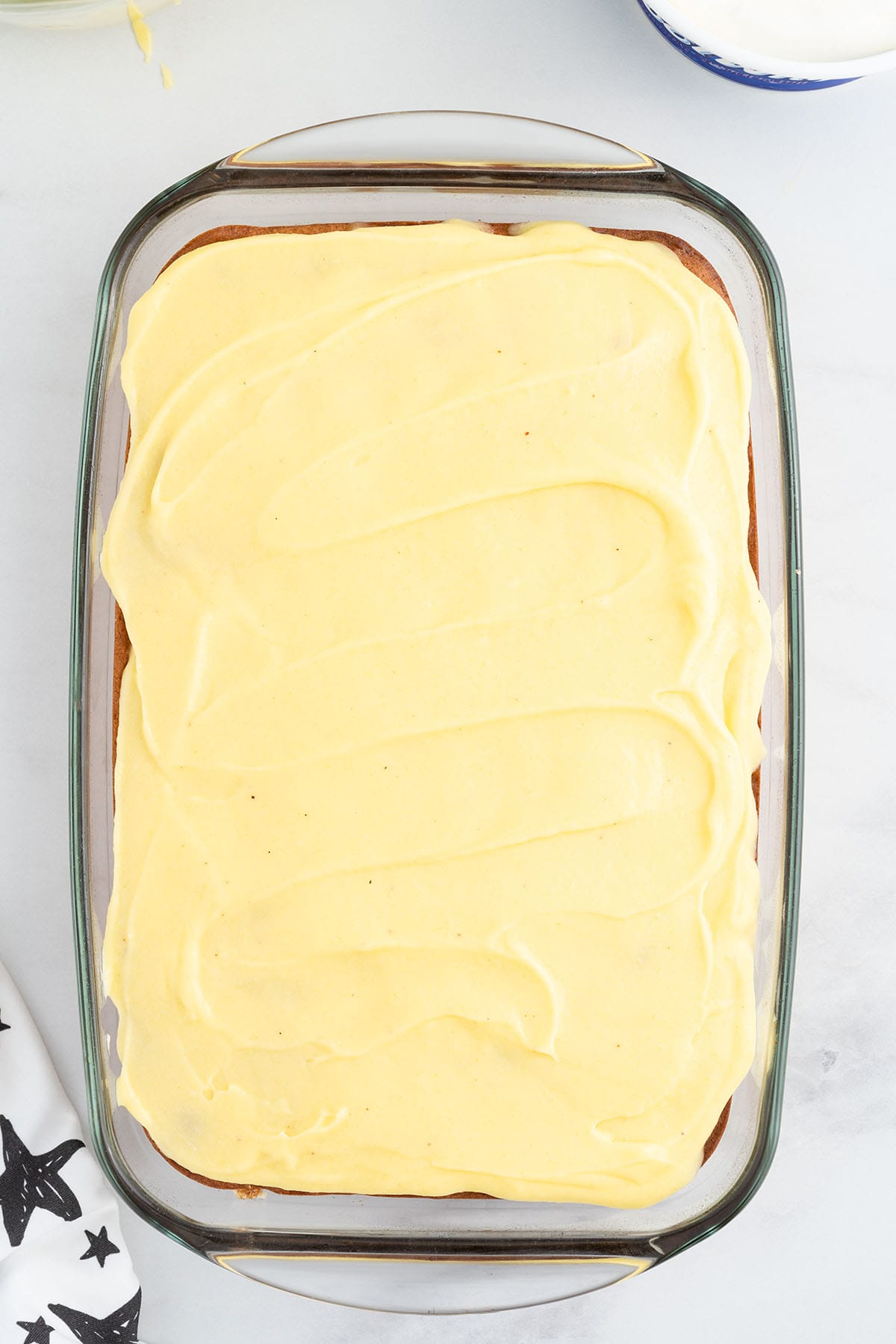Cake in a glass baking dish topped with a smooth layer of pudding.