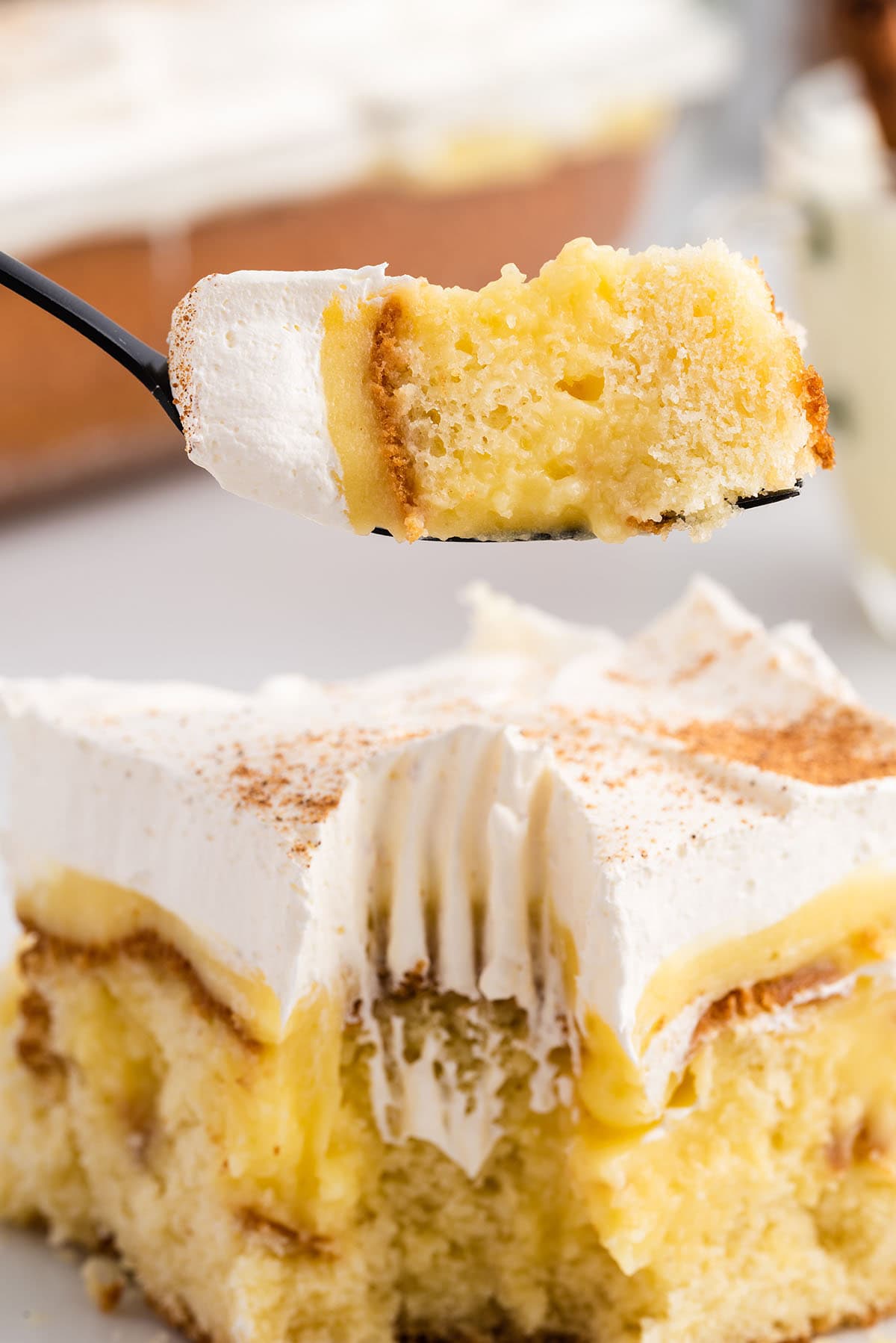 Forkful of eggnog poke cake held up close, showing the whipped cream, pudding, and moist cake layers.