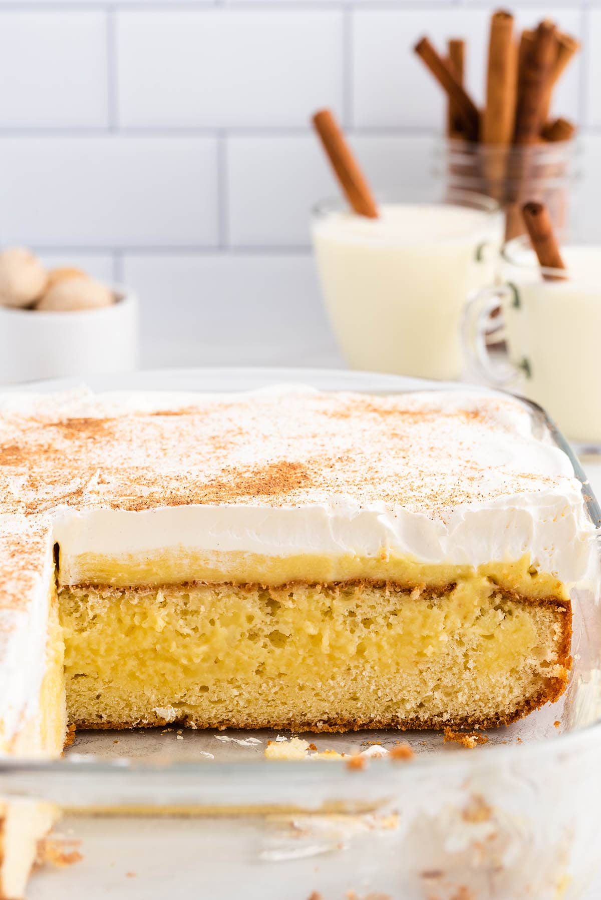 Sliced eggnog poke cake in a glass dish, showing the layers of cake, pudding, and whipped topping.