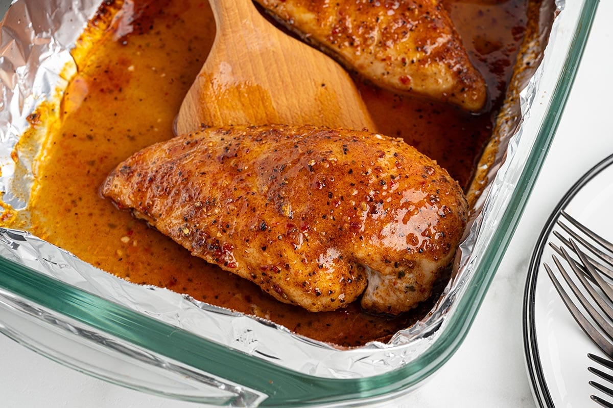 Baked Italian chicken breasts in seasoned pan juices in a foil-lined dish.