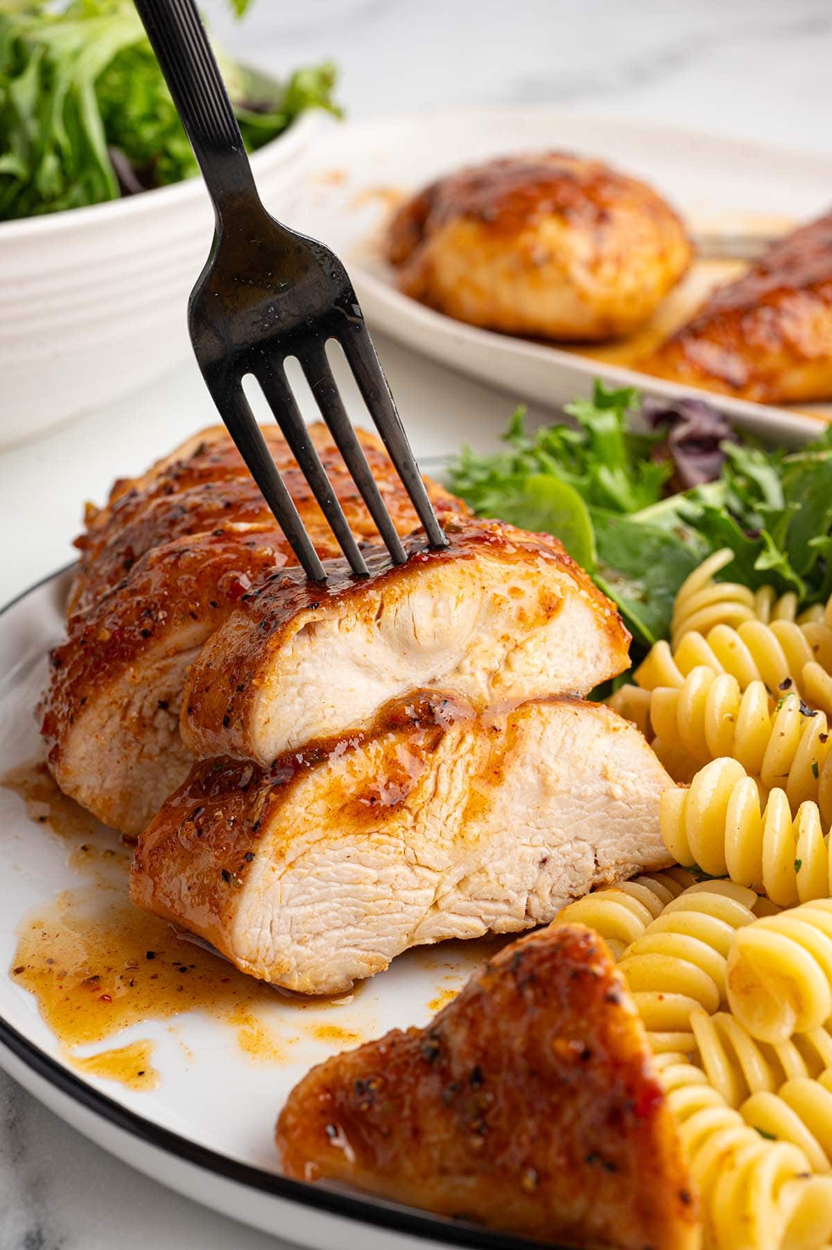 Fork in a sliced Italian chicken breast served with pasta and salad greens.