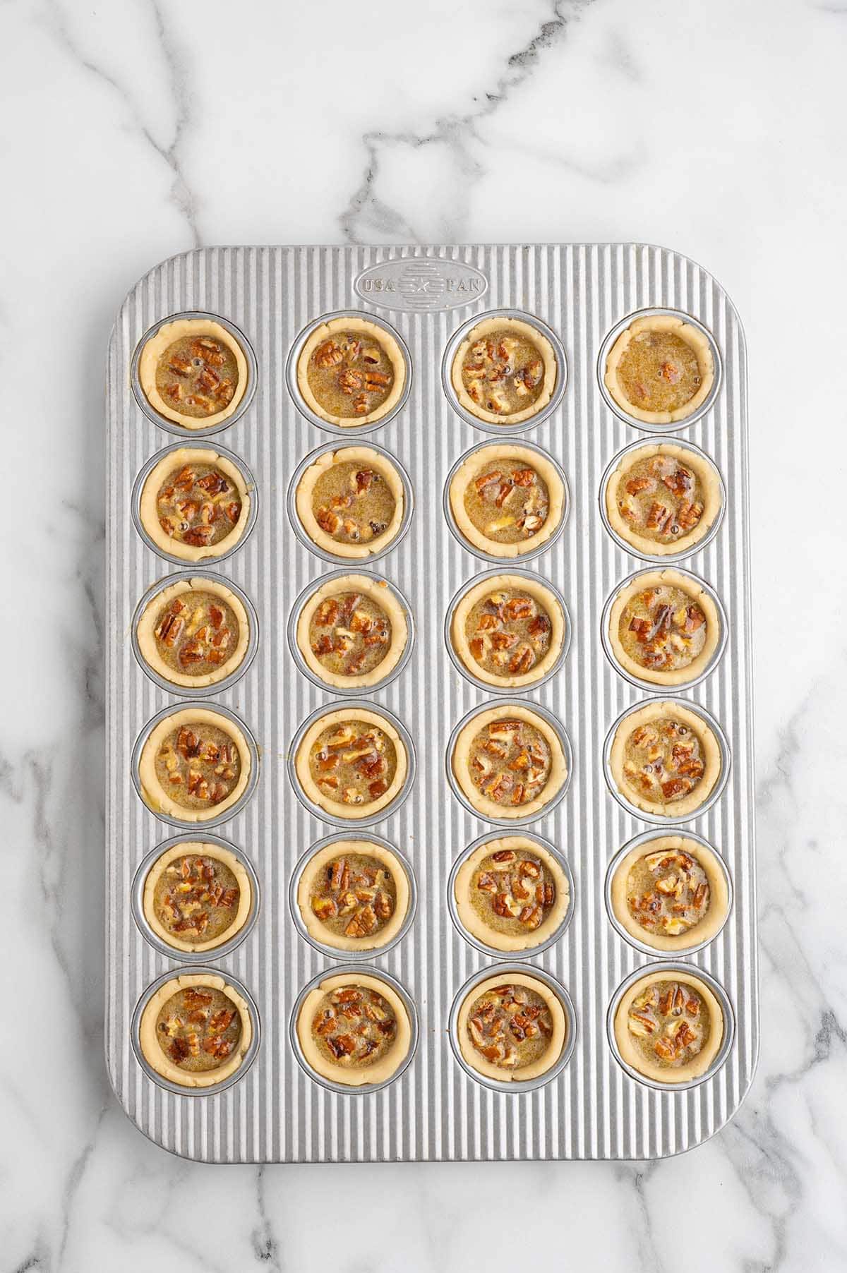 Mini pecan pies filled with pecan pie filling before baking.