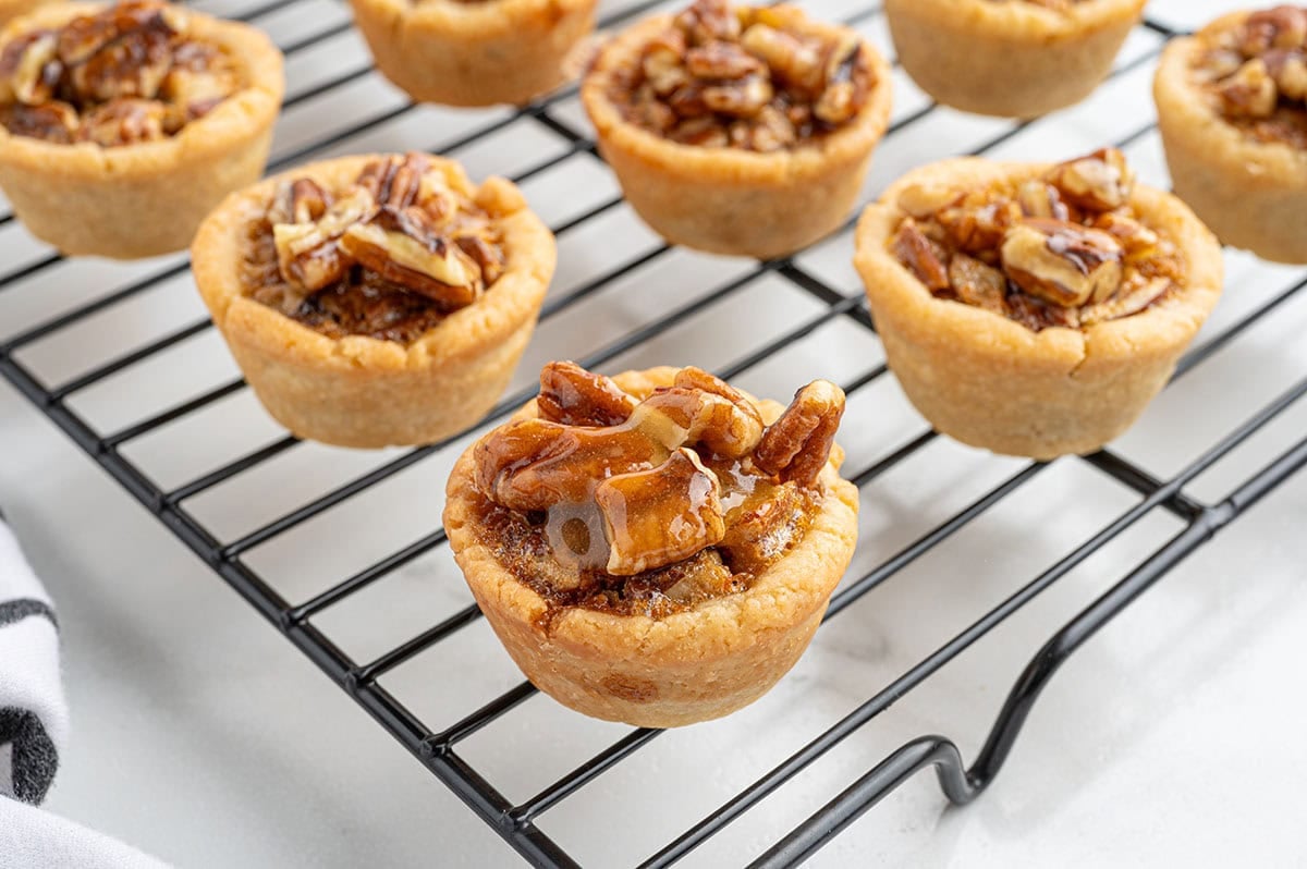 Mini pecan pies cooling on a wire rack, topped with caramelized pecans.