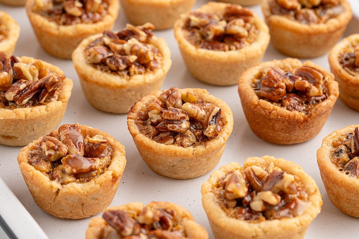 Rows of homemade mini pecan pies filled with chopped pecans and gooey caramel filling.
