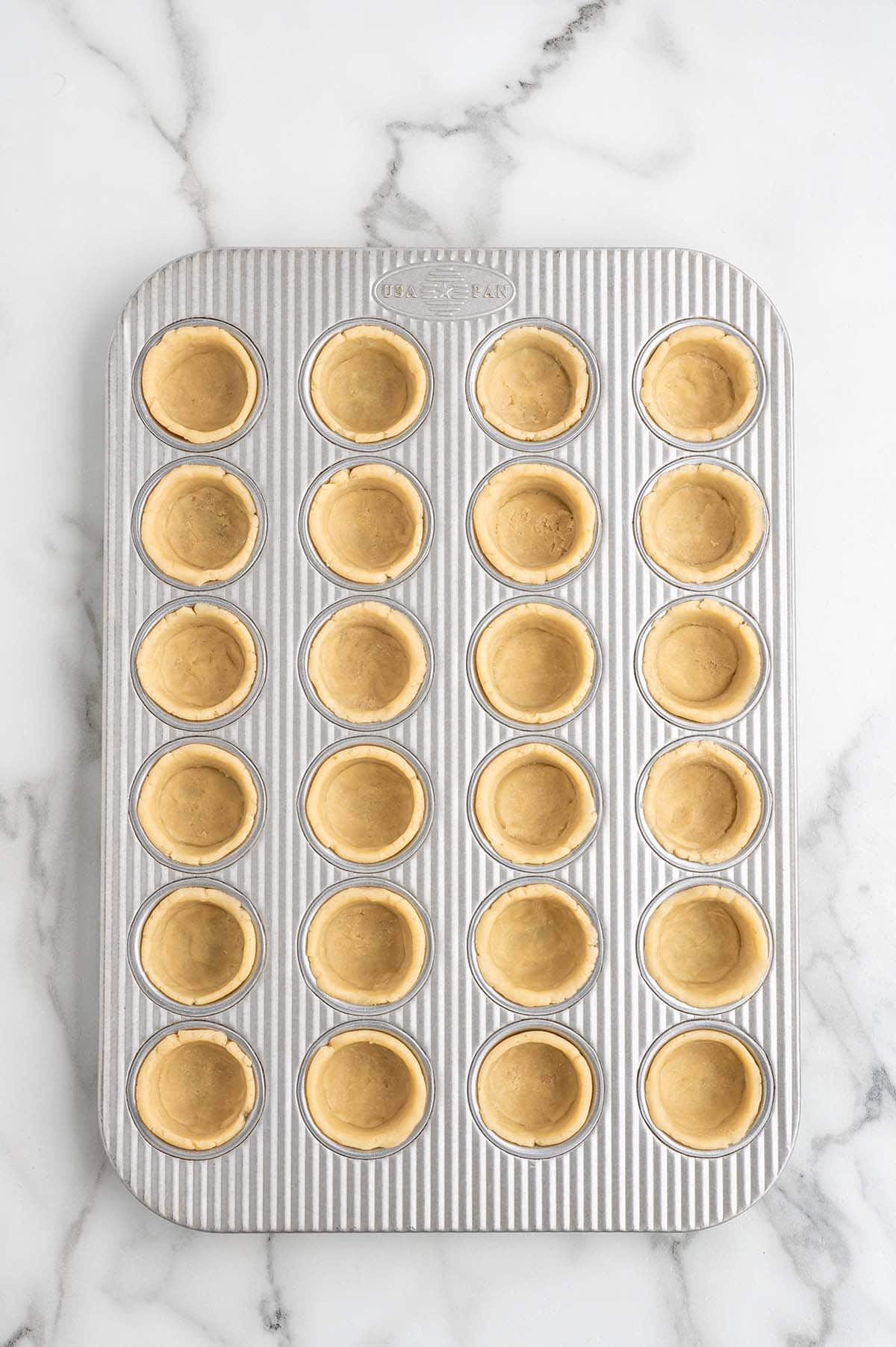 Mini pie crusts pressed into a mini muffin pan, ready to be filled.