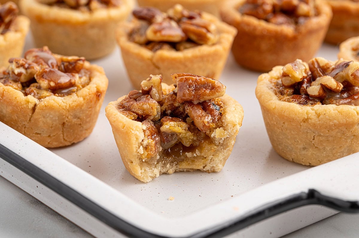 A mini pecan pie with a bite taken out, showing the gooey filling inside.