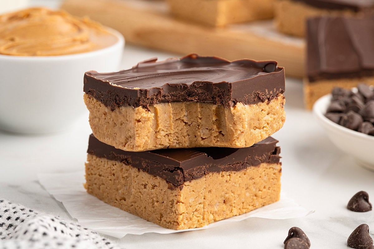 no bake peanut butter bars cut into squares and stacked on top of parchment paper. 