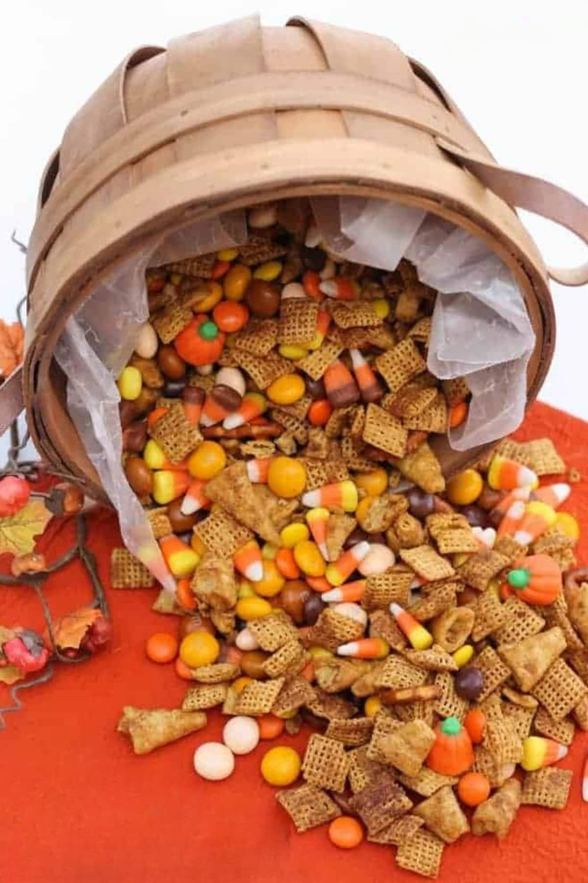 Pumpkin spice snack mix spilling out of a basket onto an orange tablecloth.