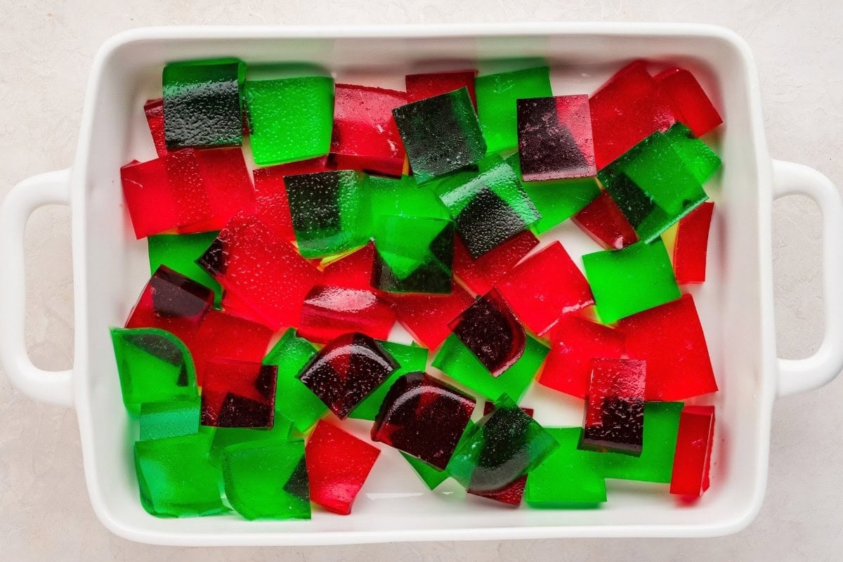 Red and green Jello cubes in a white baking dish.
