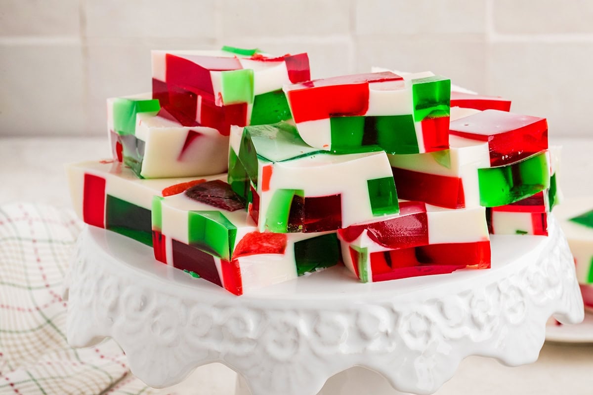 Red, green, and white Christmas Jello squares stacked on a white cake stand.