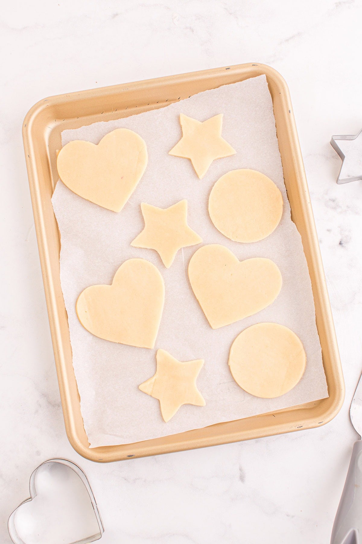 Cut out sugar cookie shapes on a baking sheet.