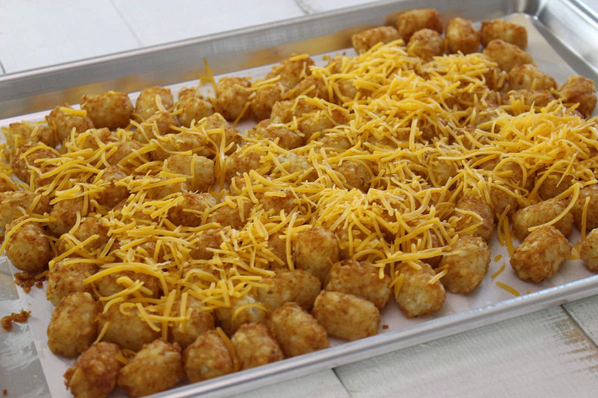 Baked tater tots topped with shredded cheddar cheese on a baking sheet.