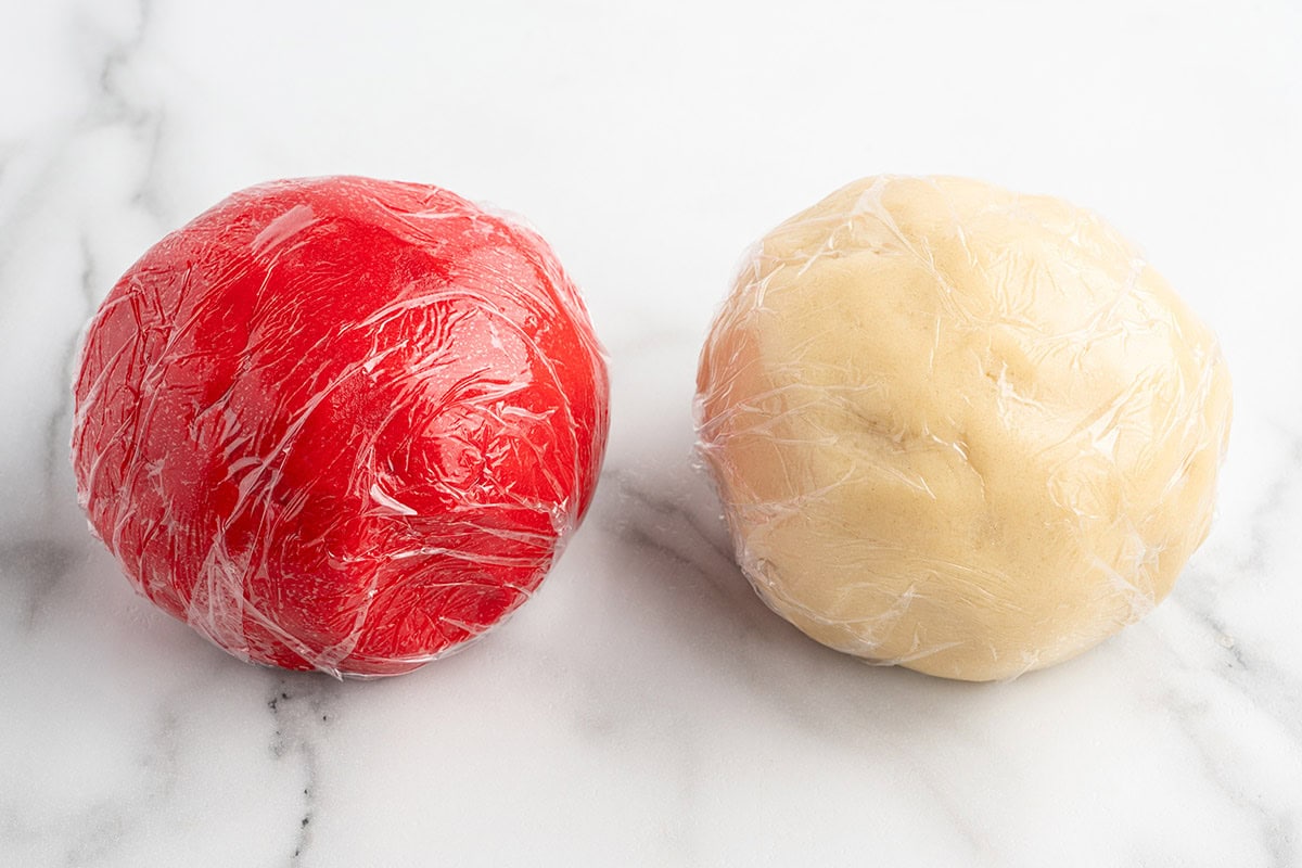 Rows of small red and plain cookie dough balls on a parchment-lined baking sheet.