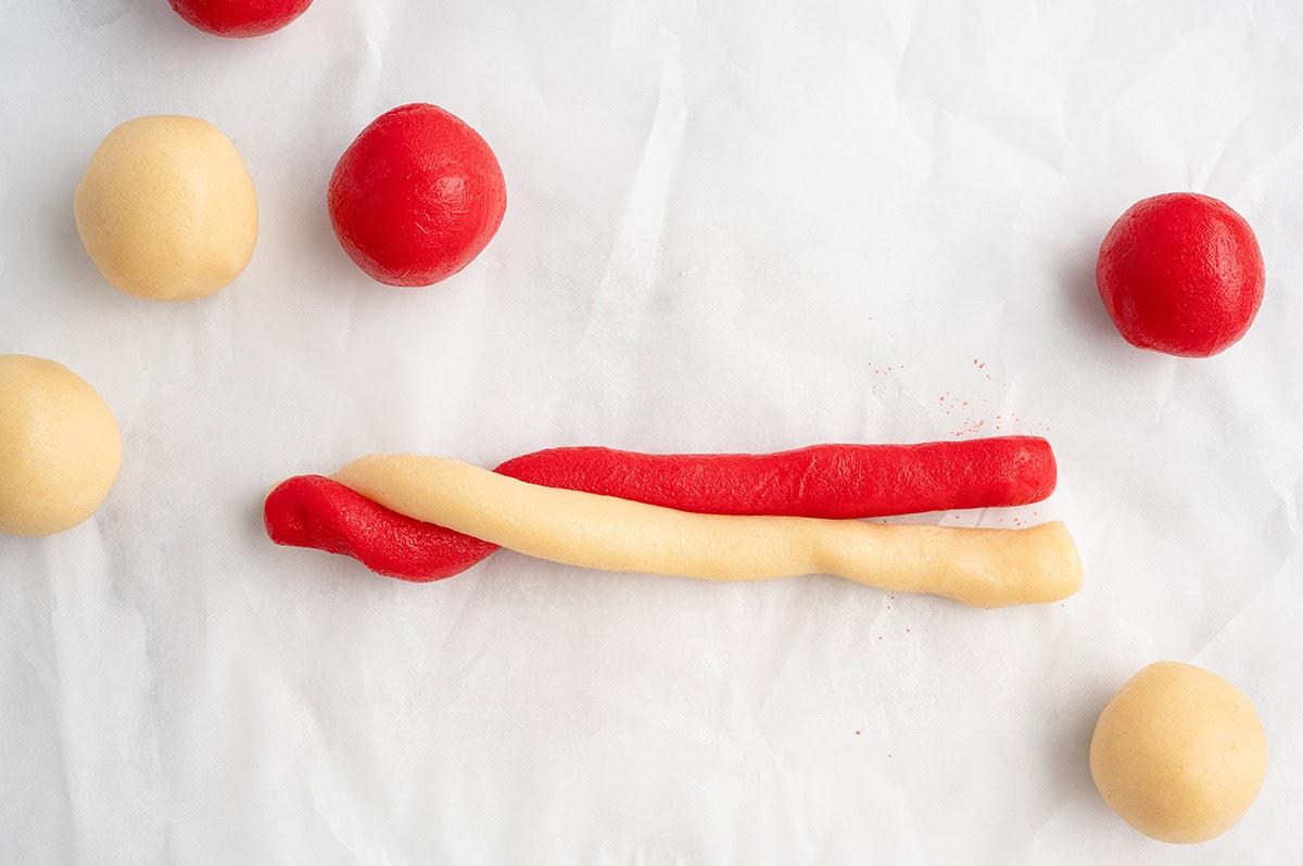 Unbaked candy cane-shaped cookies made from twisted red and white dough on a parchment-lined baking sheet.