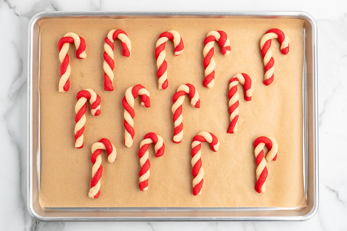 Baked candy cane cookies cooling on a wire rack next to a plate of more cookies and a wrapped gift.
