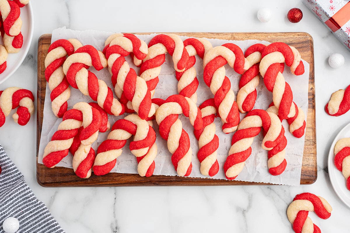 Cookie dough twisted and shaped into red and white candy canes, arranged on a wooden board lined with parchment.