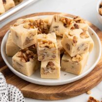 Maple walnut fudge squares stacked on a white plate.
