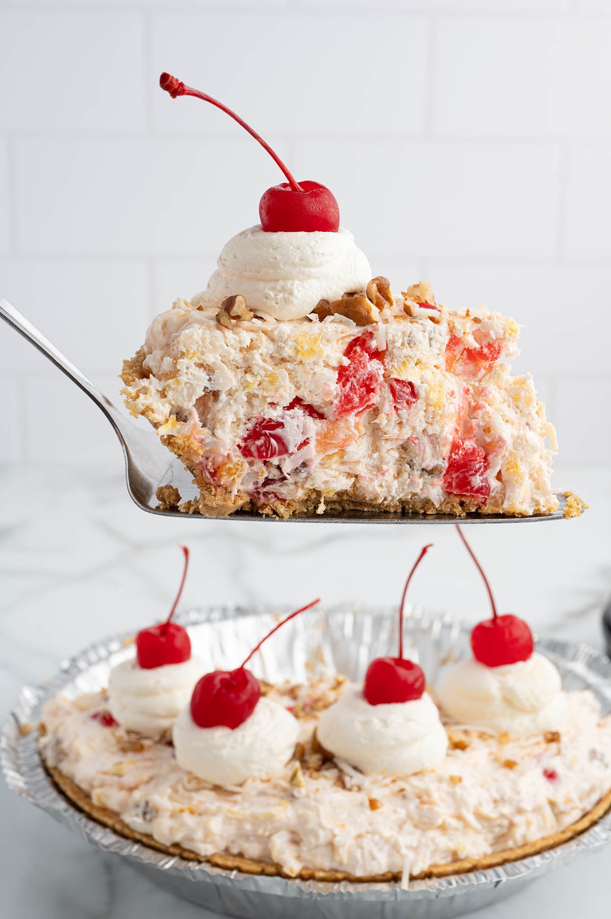 Slice of millionaire pie on a spatula topped with whipped cream, pecans, and a cherry.