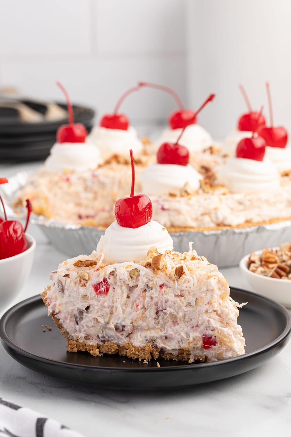 Millionaire pie slice on a black plate with whipped cream, coconut, pecans, and a cherry.