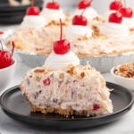 Slice of millionaire pie with creamy fruit and nut filling, topped with whipped cream and a cherry.