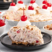 Slice of millionaire pie with creamy fruit and nut filling, topped with whipped cream and a cherry.
