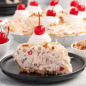 Slice of millionaire pie with creamy fruit and nut filling, topped with whipped cream and a cherry.